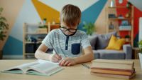 Youth education Portrait of cheerful child boy doing homework then looking at camera and smiling sitting at desk at home. Education, childhood and intellect concept. 