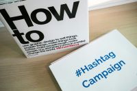 Campaign launch Desk with a how to book and a printed paper with the words #Hashtag Campaign on it 