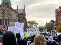 church protest On October 16, 2023, a protest demands the U.S. stop supporting Israel's genocide in Gaza. A dense crowd at Copley Square fills the street with umbrellas and keffiyehs, their handmade signs rising against the gray sky. Messages like “75 years of oppression is not unprovoked,” “Free all Palestinian political prisoners,” and “This is not war, it’s genocide” express collective outrage and grief over decades of U.S. complicity in Palestinian displacement and Israeli occupation. 