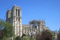 Building collapsed Notre Dame five days after the fire of 15 April 2019. The roof and spire have collapsed and the carved stone walls are charred. The remains of melted metal scaffolding remain atop the cathedral where the roof and spire were. A crane helps support a leaning bell tower. It's a sunny day with clear blue skies. notre dame,france,paris