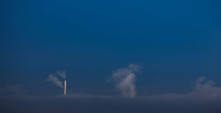 Pollution control A solitary smokestack stands tall, emitting a plume of smoke into the vast blue sky, with sparse clouds scattered across the frame. climate change,environmental issue,clear sky