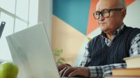 retirement education Portrait of serious old man working with laptop computer indoors in house sitting at table in room. Modern technology, retired people and information concept. 