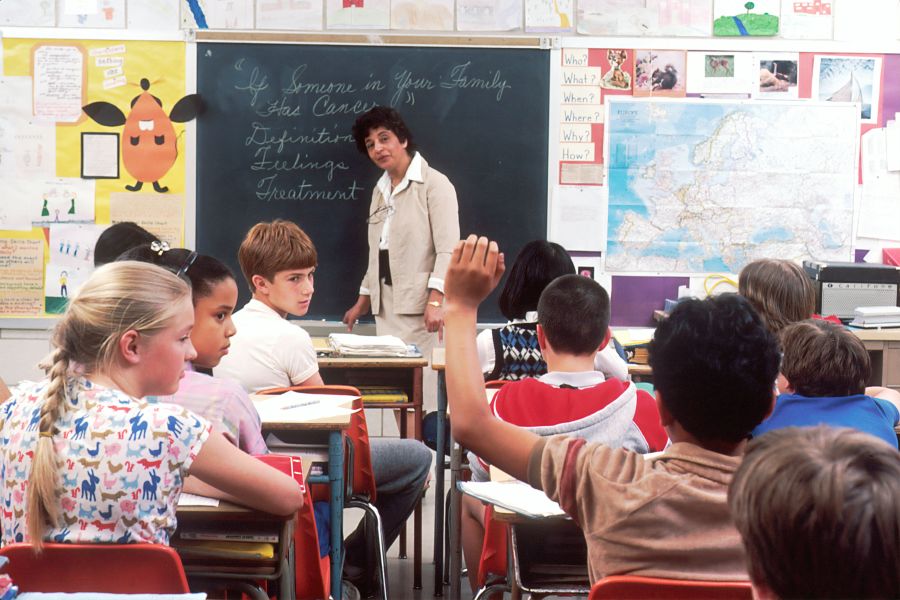 Teacher Children in a Classroom. In the back of a classroom, are children about 11 years old with a female teacher talking about the subject - If Someone in Your Family Has Cancer. Photographer Michael Anderson 